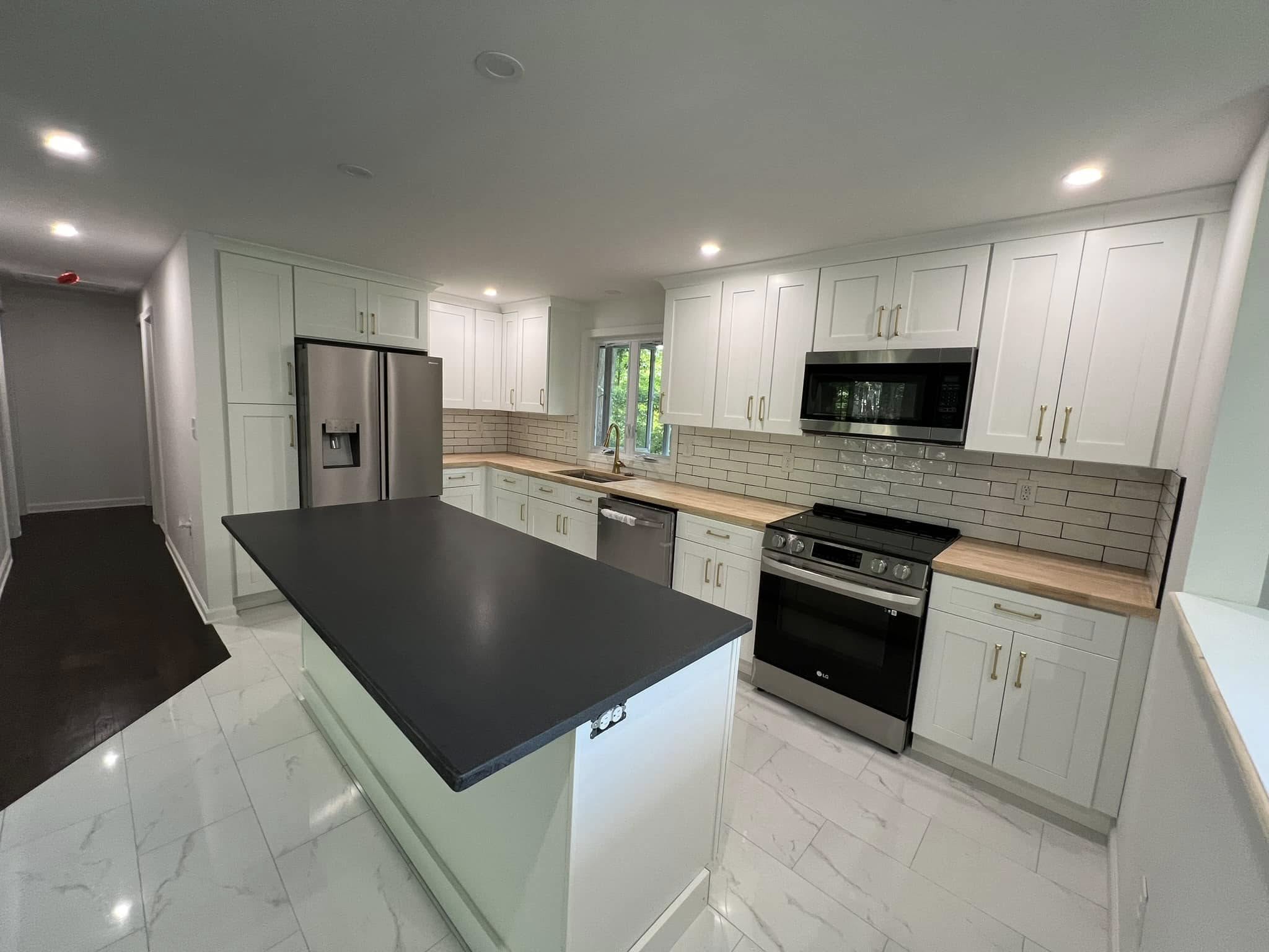 Modern kitchen with white shaker cabinets, light wood countertops, and stainless steel appliances. Features a black countertop island, subway tile backsplash, and recessed lighting. The kitchen has a clean, bright design with white marble-look tile flooring. Located in Andover, Connecticut.